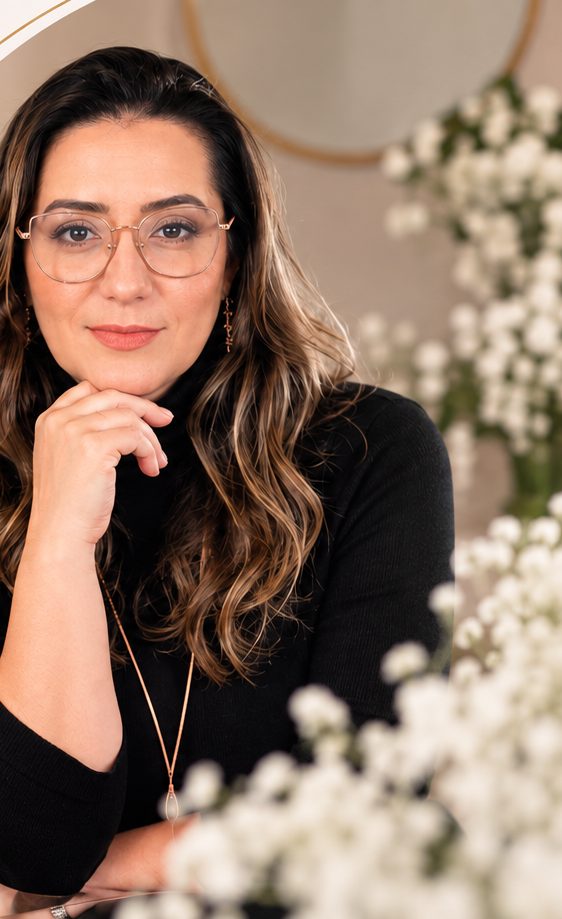 Luiza Paiva com a mão no queixo, ao lado de flores brancas