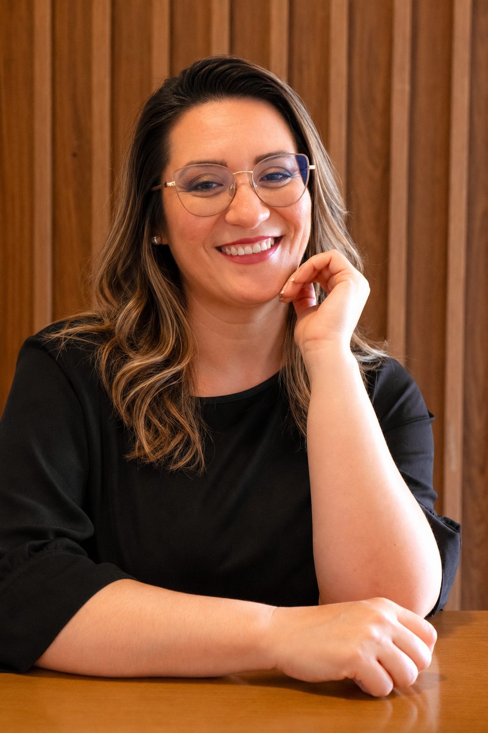 Luiza Paiva, cerimonialista em Mafra, sorrindo apoiada em uma mesa de madeira